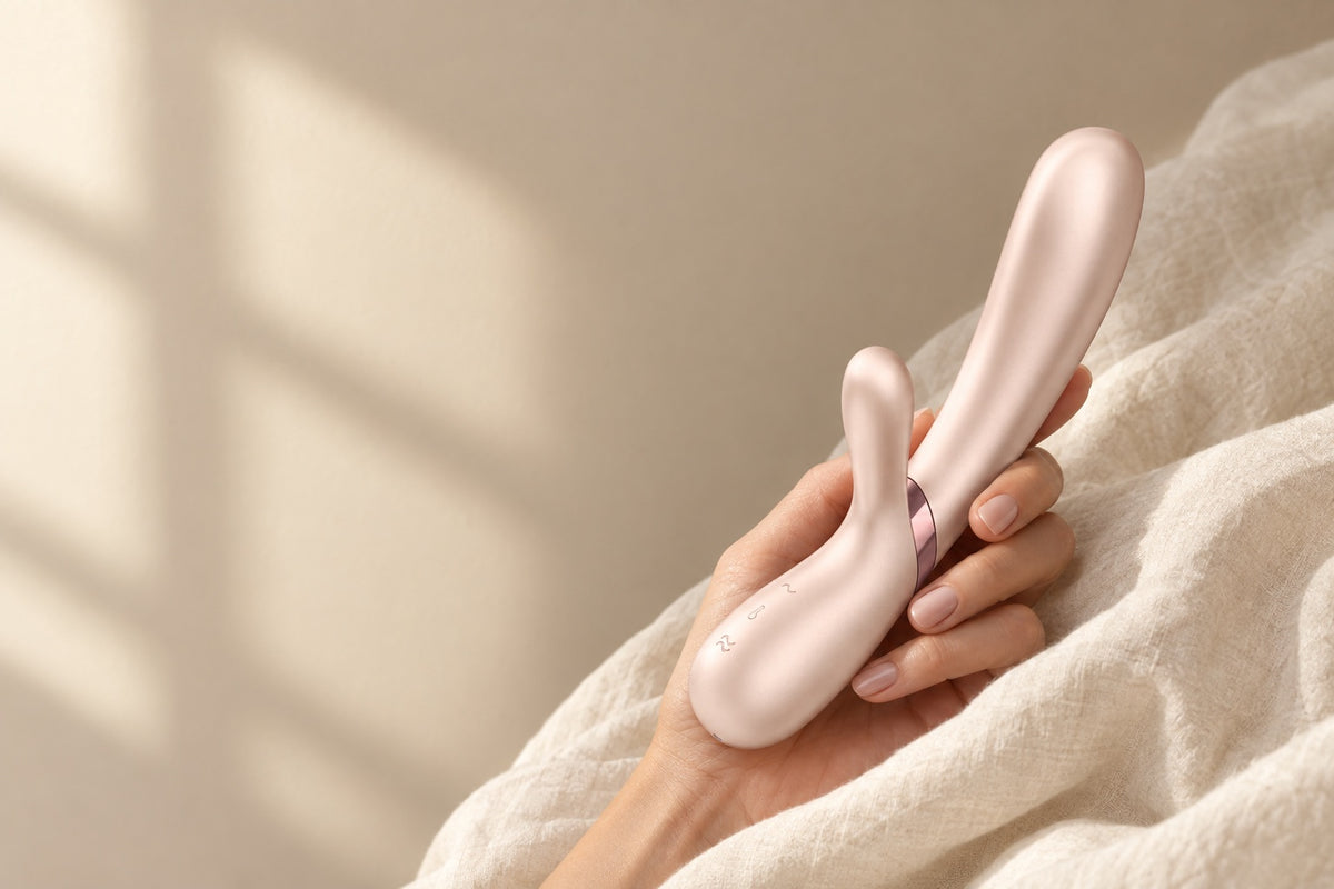 Mano sosteniendo el vibrador Satisfyer Hot Lover entre sábanas de lino